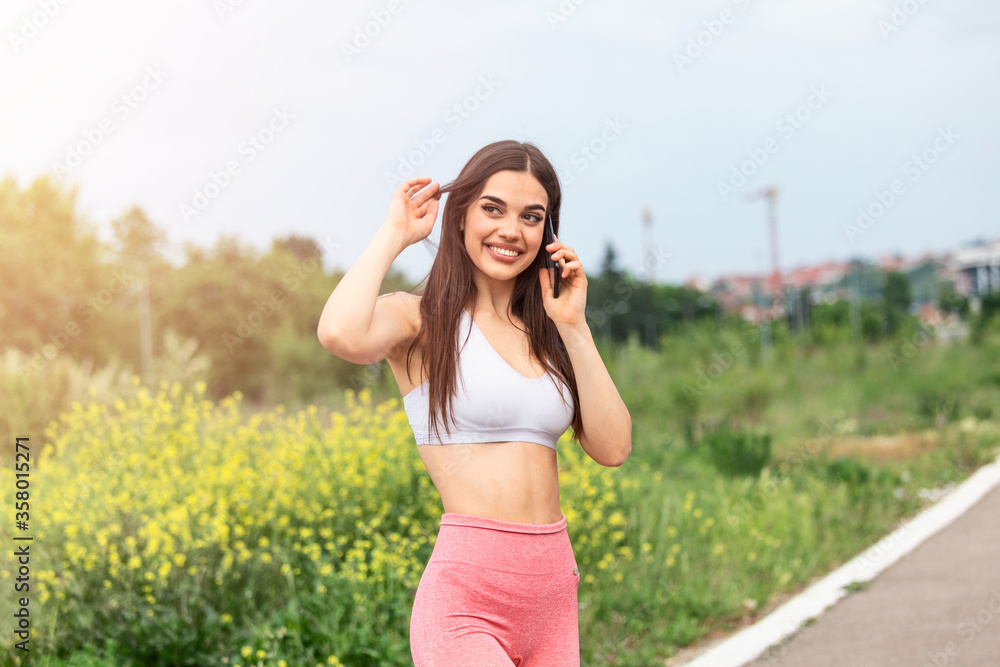 Portrait of a young woman in sportswear talking on phone outdoors while taking break between training, Portrait of a young woman in sportswear talking on phone outdoors while taking break between training,
