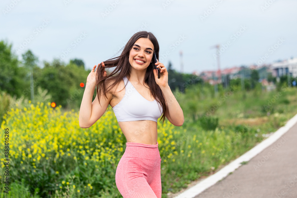 Portrait of a young woman in sportswear talking on phone outdoors while taking break between training,