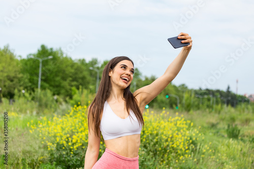 Young Sporty Woman Taking a Selfie at Park. She is Looking at Camera. An attractive female runner taking selfie outside.