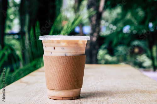 Cold coffee in plastic cup on wooden table at coffee shop. Paper mock up on latte with copy space. Vintage filter