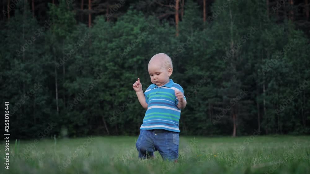 Funny Small Kid In Learns To Doing First Steps And Falls On Green Lawn Funny Small Kid In Learns To Doing First Steps And Falls On Green Lawn
