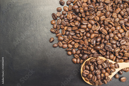 Wooden spoon with dark roasted coffee beans on blackboard background. Photos from the top view and copy space. Seed nature from the above view. Group agriculture grain arabica. © Chaiyaphruek