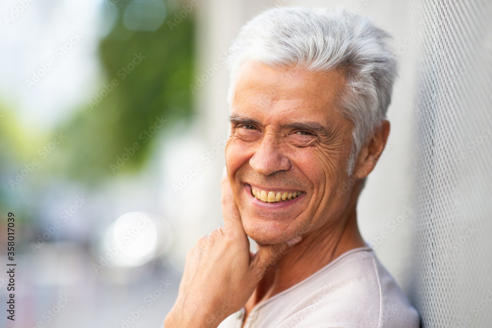 Close up handsome older man smiling with hand to chin outside Close up handsome older man smiling with hand to chin outside