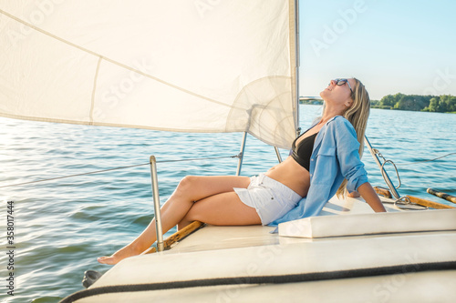 Young happy woman enjoying sunset from deck of sailing boat moving in sea at evening time. Travel, Summer, Holidays, Journey, Trip, Lifestyle, Yachting concept.