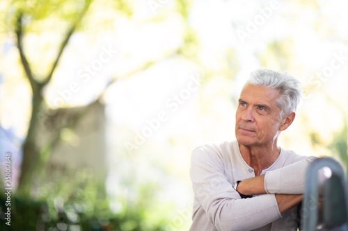 handsome elderly man sitting on park bench looking away