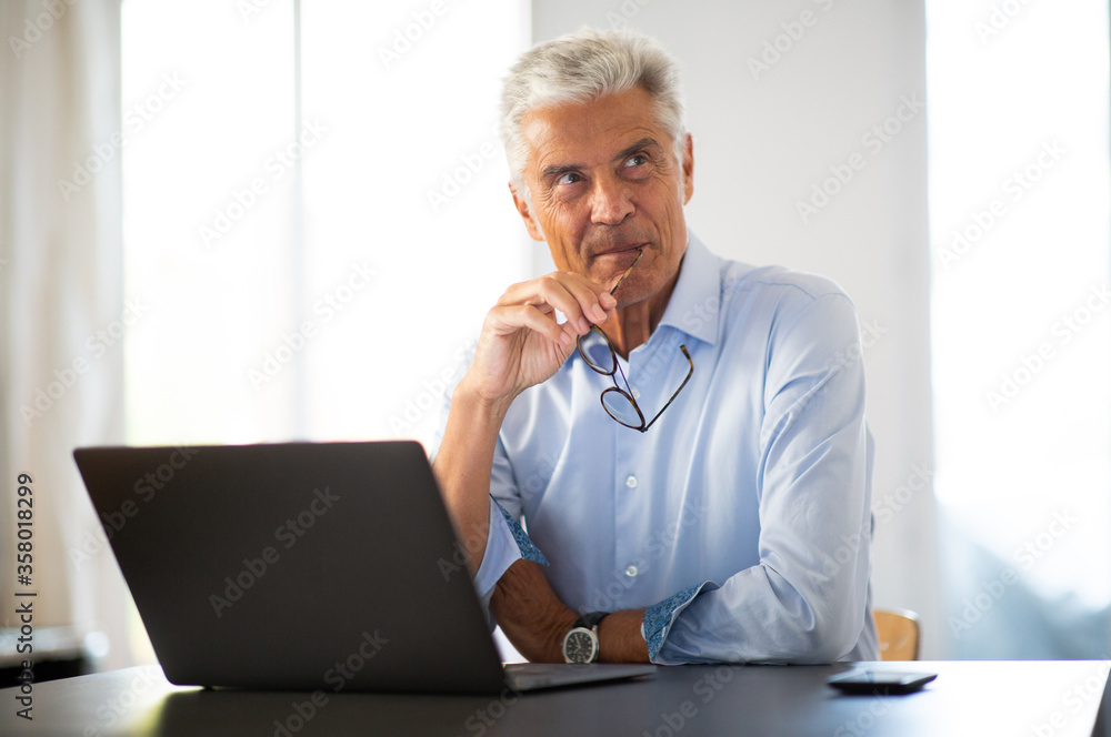 businessman sitting at office desk with laptop and looking away thinking businessman sitting at office desk with laptop and looking away thinking