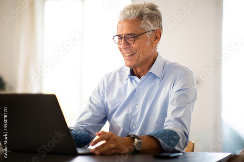 Wallpaper Mural smiling older man sitting at home looking at laptop computer Torontodigital.ca