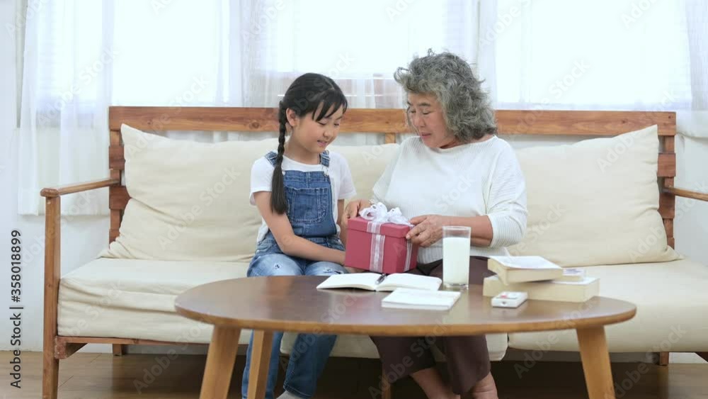 Asian grandmother receive gift box from her Asian granddaughter in living room. Asian grandmother receive gift box from her Asian granddaughter in living room.