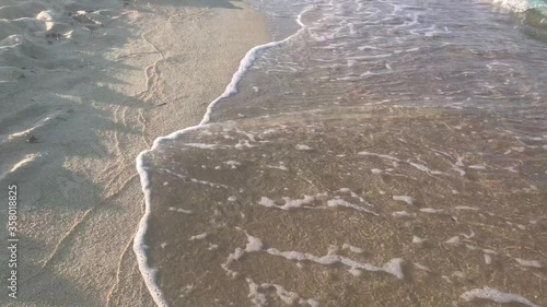 Faceless video of walking on clean sandy beach with waves crashing onto beach  in 4k photo