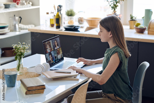 Fotografie Focused teenage girl sitting at table and using laptop while improving skills at
