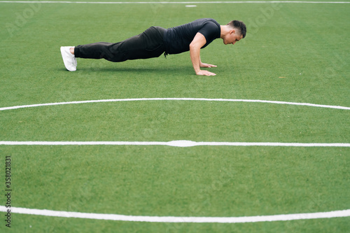 Athletic man doing push ups on green grass on the playground of the stadium. The concept of active sports alone is determined by the coronavirus