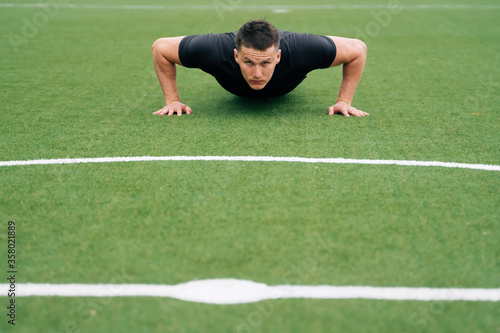 Portrait of a young male athlete in black clothes doing push-ups, look at the camera. The concept of online education of small business