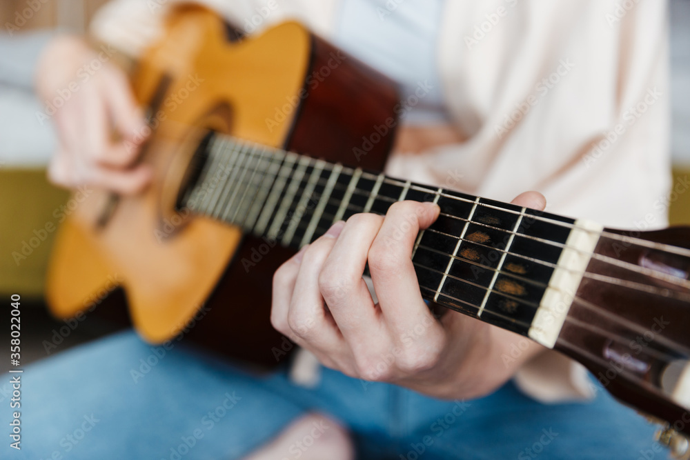 Image closeup of young caucasian woman playing acoustic guitar at home