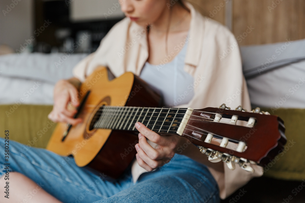 Image of young caucasian woman playing acoustic guitar at home