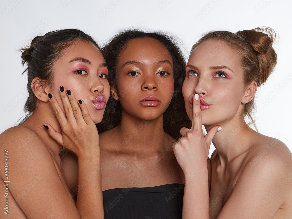 The real beauty exists in every corner of the world and is presented by women of all races. Three beautiful ladies with different skin and hair colour are making faces on the grey background. The real beauty exists in every corner of the world and is presented by women of all races. Three beautiful ladies with different skin and hair colour are making faces on the grey background.