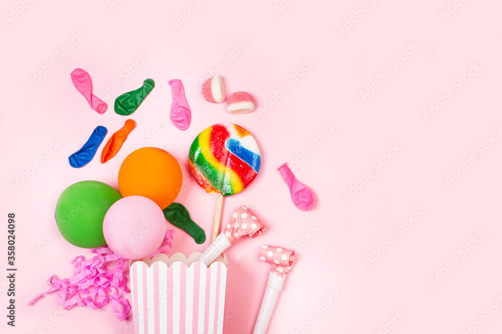 Caja de cumpleaños con globos, piruletas de colores y confeti sobre un fondo rosa liso y aislado. Vista superior. Copy space