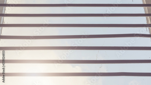 horizontal black jalousie planks against bright sunlight spot and clear blue sky