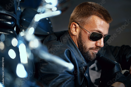 Bild auf Leinwand Cool man biker in sunglasses sitting near his motocycle