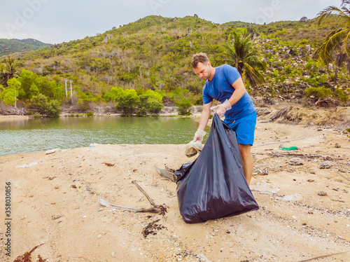 Man in gloves pick up plastic bags that pollute sea. Problem of spilled rubbish trash garbage on the beach sand caused by man-made pollution and environmental, campaign to clean volunteer in concept