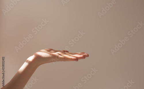  Female hand holds copy space and some object on a white background with beautiful shadows. Layout and frame in the sun