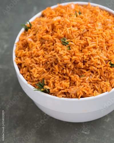 A big white bowl filled with tasty Nigerian Jollof Rice served and decorated with some green spices