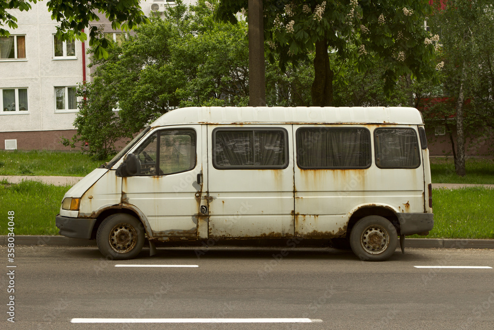 White rusty abandoned compact van. Unnecessary malfunctioning car junk truck abandoned on the side of the road in the industrial part of the city.