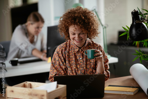 Young businesswoman drinking coffee in her office. Happy woman working on lap top.