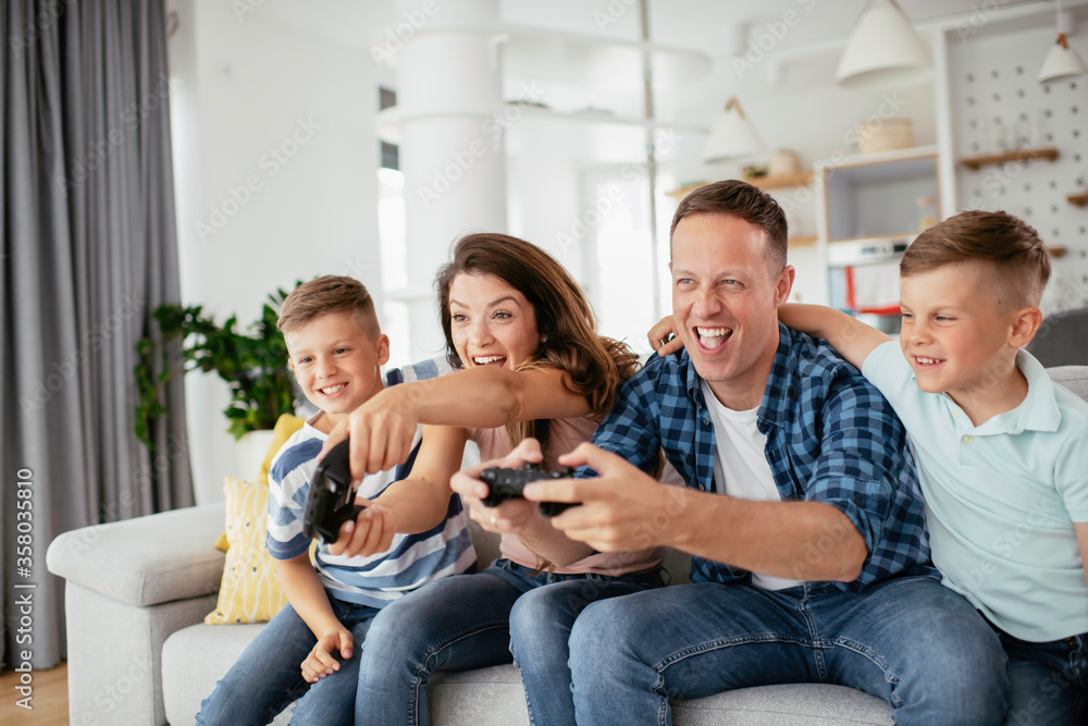 Husband and wife playing video games with joysticks in living room. Loving couple are playing video games with kids at home. Husband and wife playing video games with joysticks in living room. Loving couple are playing video games with kids at home.