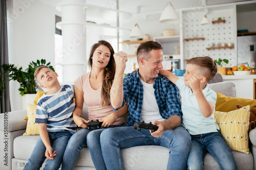 Husband and wife playing video games with joysticks in living room. Loving couple are playing video games with kids at home.