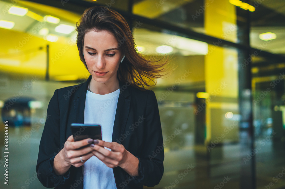 portrait professional female finance lawyer standing near office in evening street communicates online by cellphone. successful businesswoman pushing message to colleagues on mobile yellow neon lights