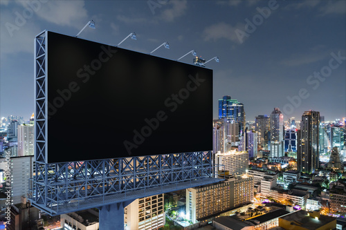 Blank black road billboard with Bangkok cityscape background at night time. Street advertising poster, mock up, 3D rendering. Side view. The concept of marketing communication to promote idea.