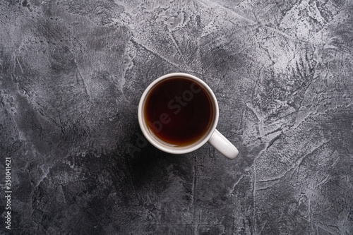 One ceramic cup with hot black tea, drink in white teacup on textured dark stone background, top view