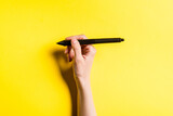Cropped view of designer holding stylus of graphics tablet on yellow background