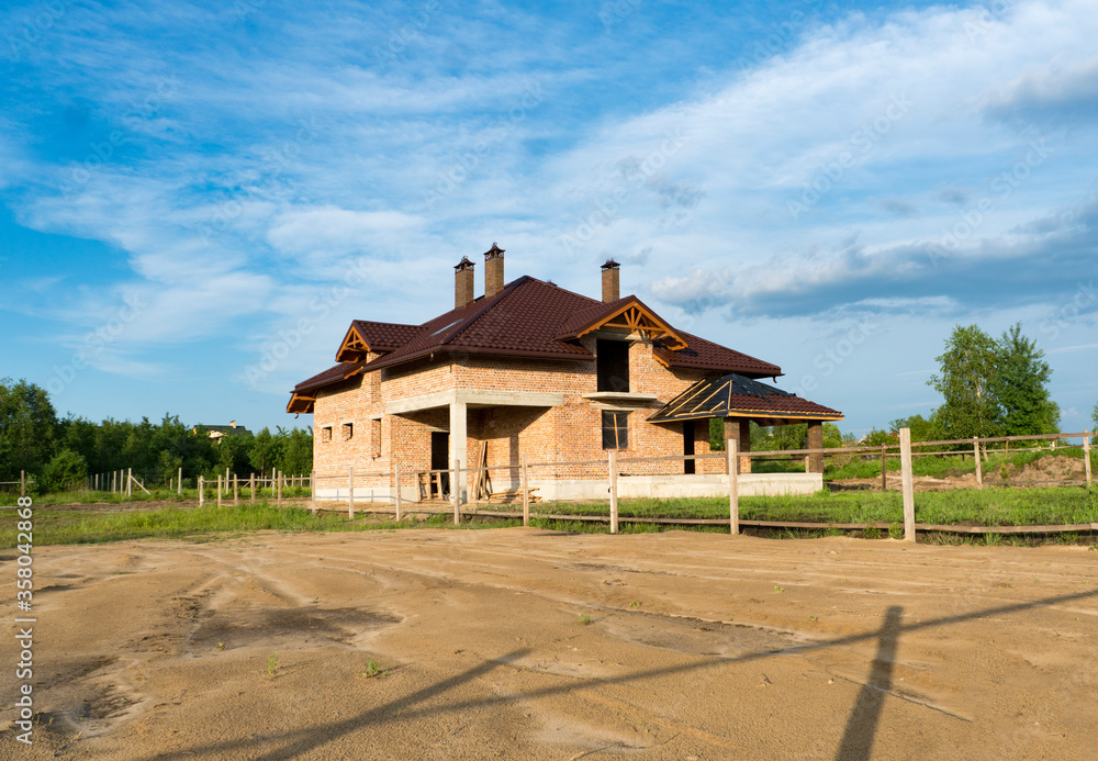 Construction of brick family house in suburbs. Shell of town home with completed walls and roof. Building a home in the field.