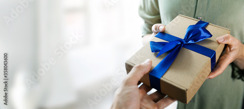 hand giving gift box with blue ribbon to a woman. copy space