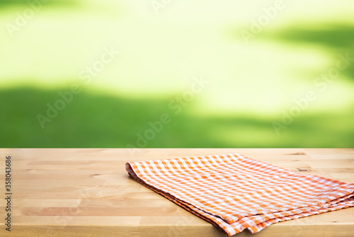 Checked,tablecloth on wood with blur green courtyard background.Summer and picnic concepts