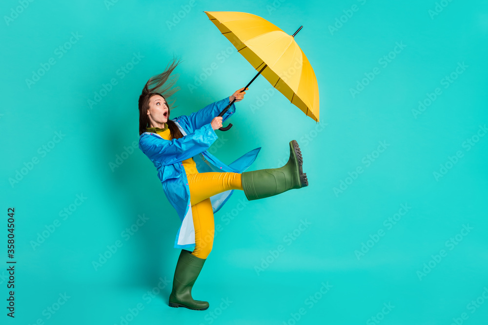 Full length profile photo of shocked lady stormy rainy weather walk street hold umbrella catch strong wind blew away wear raincoat sweater pants gumboots isolated teal color background - obrazy, fototapety, plakaty 