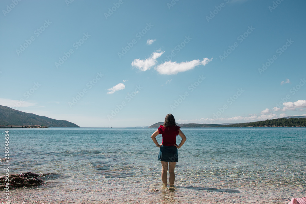 Woman seen from behind entering the sea clothed. Standing in clear beautiful sea on the island of hvar, beaches of Starigrad. Mountains and endless sea in the distance