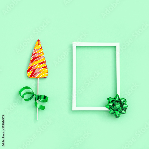 Color candy creative for New Year or Christmas. Lollipops shaped like Christmas tree and and white frame with copy space on neo mint colored paper background. Top view. photo