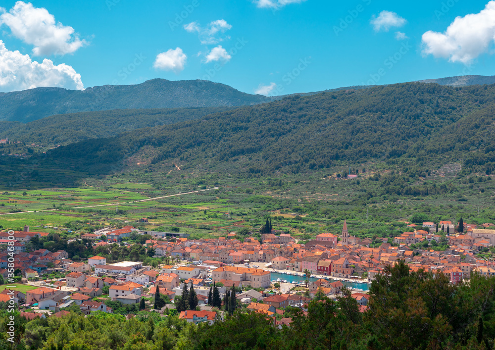 Picturesque panorama of Starigrad town on the island of Hvar. Seen from a nearby hill. Old church belltower rising above the buildings, town surrounded by endless green fields and mountains