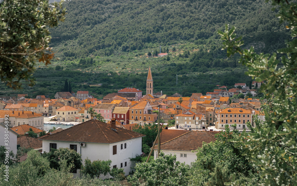 View of the old house roofs of the town of Starigrad on the island of Hvar. Church belltower rising above the buildings. Green lush foliage and mountains behind it