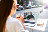 Video call outdoors. A young woman sits in the summer cafe and uses laptop for video connection with a friend, coworker, she talks with an african-american guy