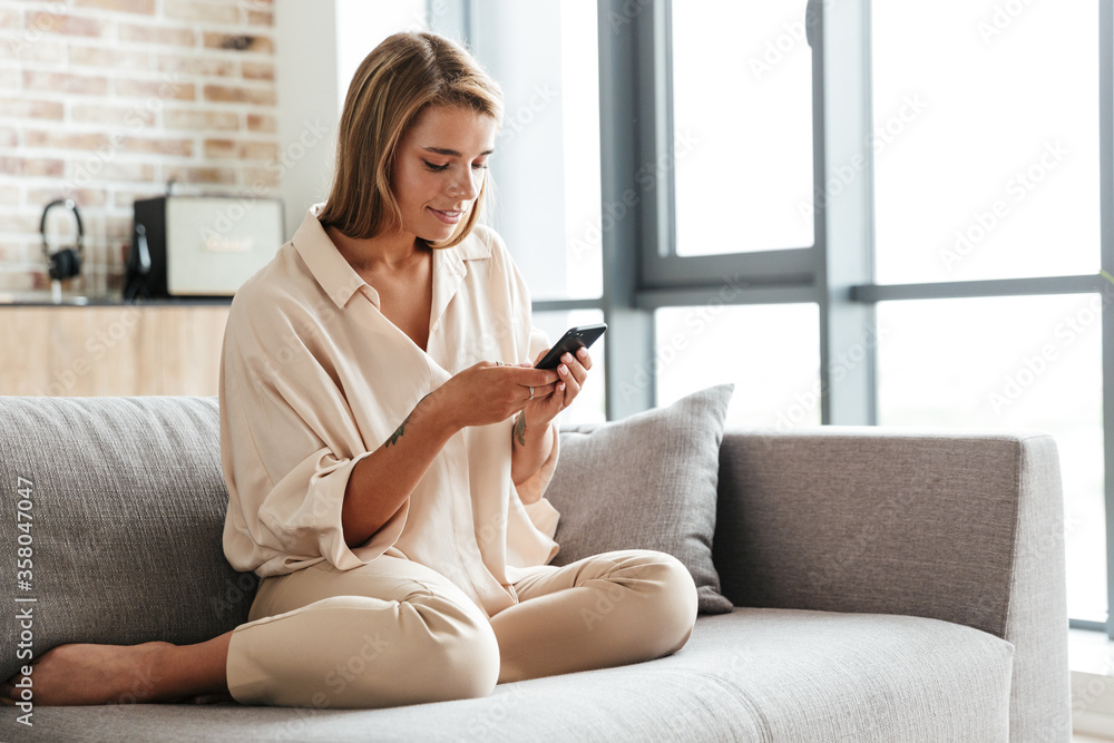 Image of woman smiling and using cellphone while sitting on couch Image of woman smiling and using cellphone while sitting on couch