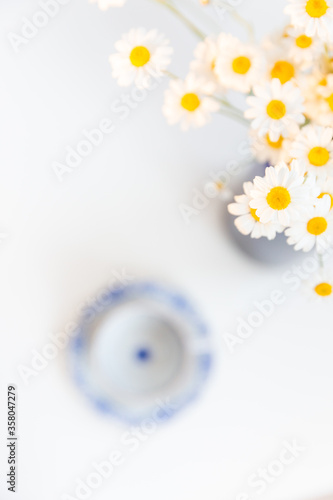 Bouquet of daisies and vintage tea cup on white background. With copy space. Cup of aromatic tea with a camomile flowers. Place for text. 