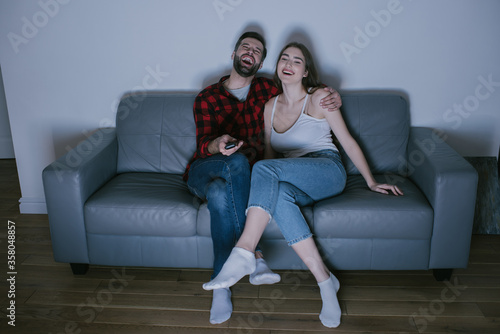 cheerful couple laughing while watching tv on sofa at home