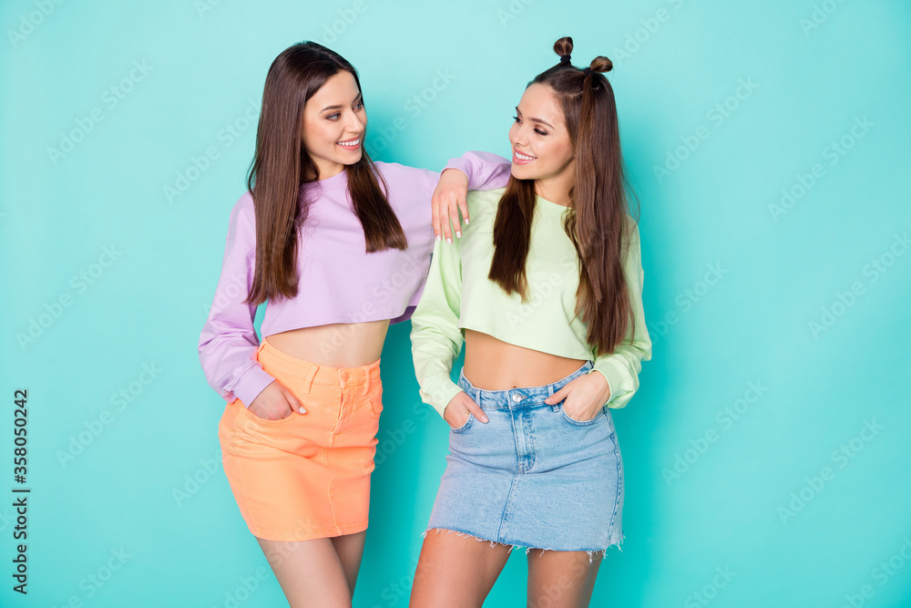 Photo of two cheerful lady best friends cool youth look clothes talking communicating wear cropped sweaters pullovers naked belly short skirts isolated pastel teal color background