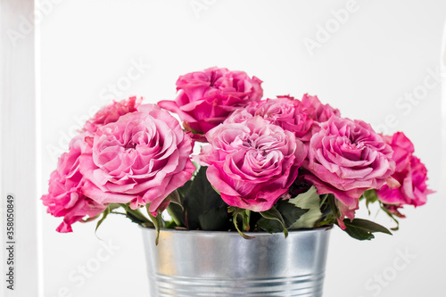 Bouquet of red roses in a tin bucket on a white wall background.