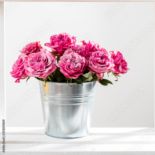 Bouquet of red roses in a tin bucket on a white wall background. © elenarostunova