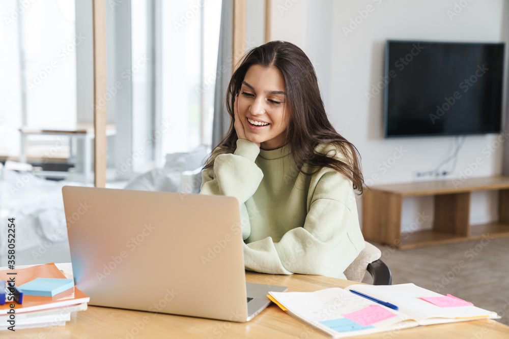 Photo of cheerful student woman using laptop while doing homework Photo of cheerful student woman using laptop while doing homework