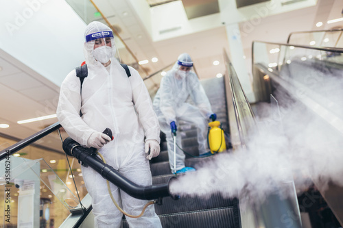 Professional workers in hazmat suits disinfecting indoor of mall, pandemic health risk, coronavirus photo